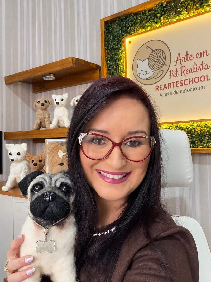 Renata segurando um pug feltrado junto ao rosto, no ateliê